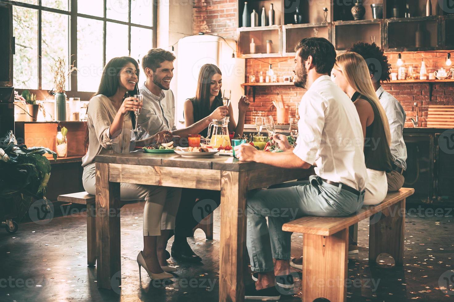 Dinning with best friends. Group of cheerful young people enjoying dinner while sitting on the kitchen together photo