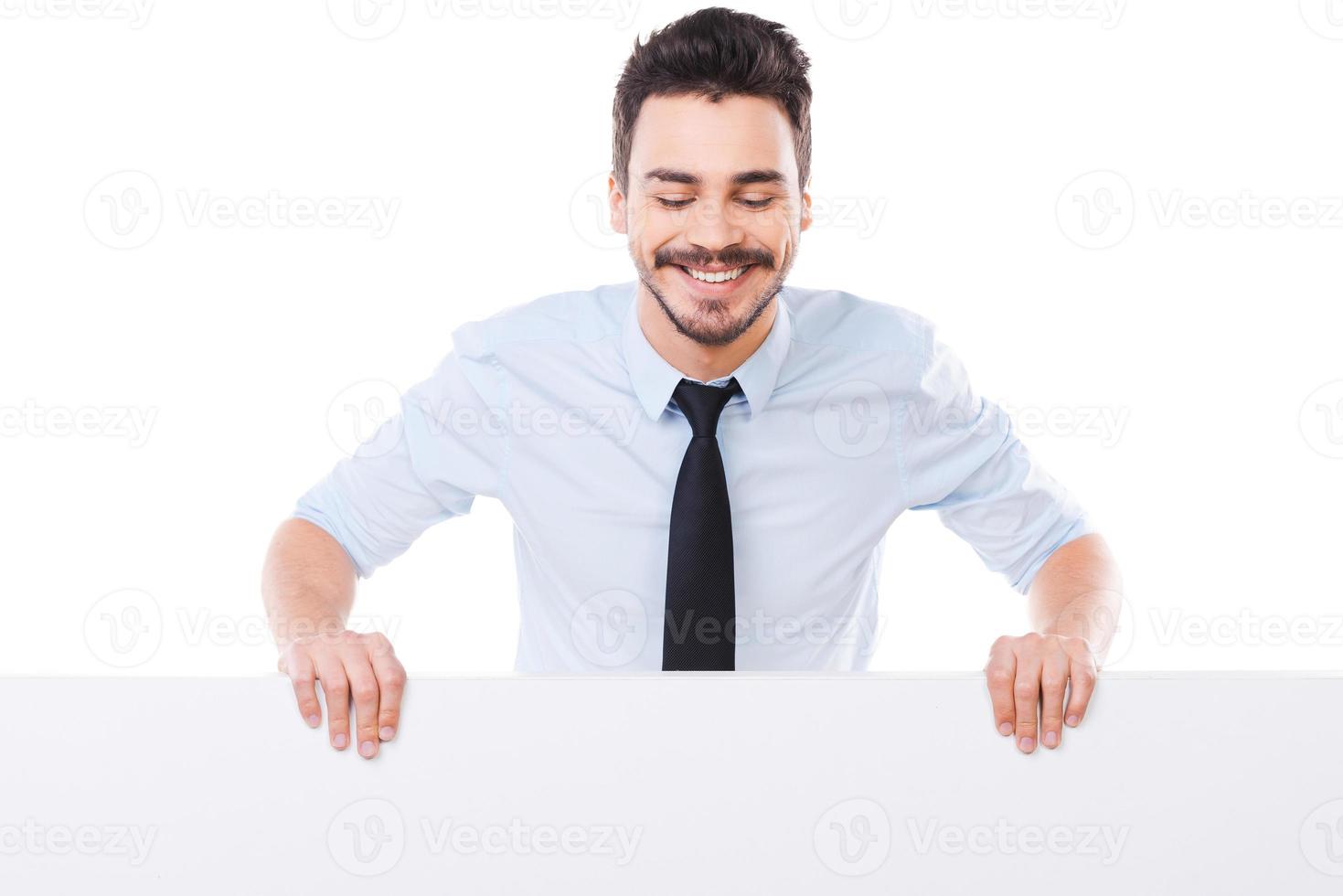 Curious businessman. Handsome young man in shirt and tie leaning at the copy space and looking at it with smile while standing against white background photo