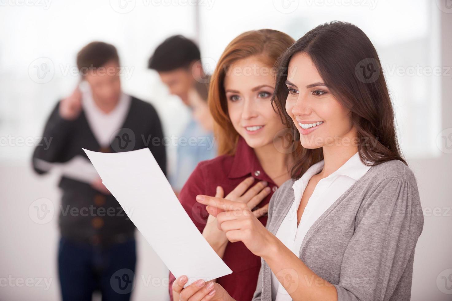 Discussing a good condition contract. Two beautiful young women discussing document while two men communicating on background photo