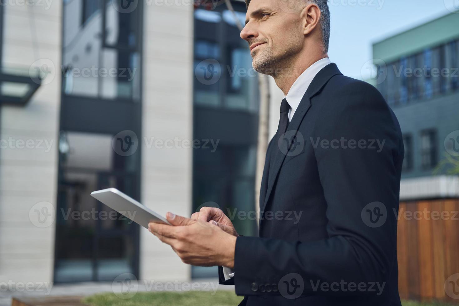 Confident mature businessman using digital tablet while standing outdoors near office building photo
