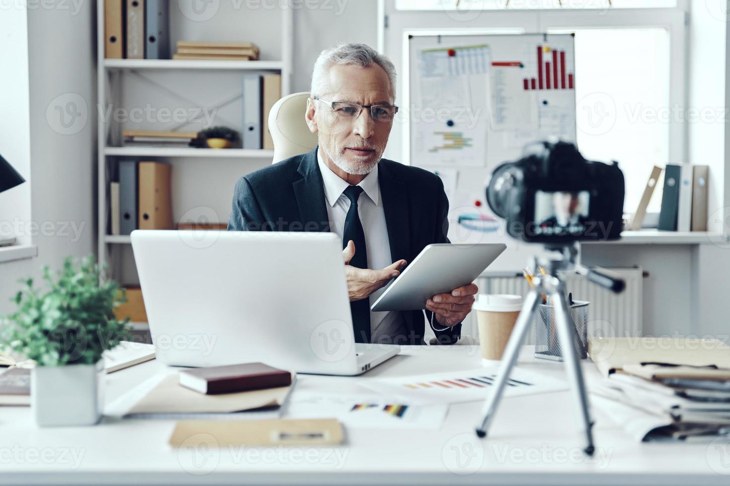 un anciano con un elegante traje de negocios que usa una tableta digital mientras hace un video en las redes sociales foto