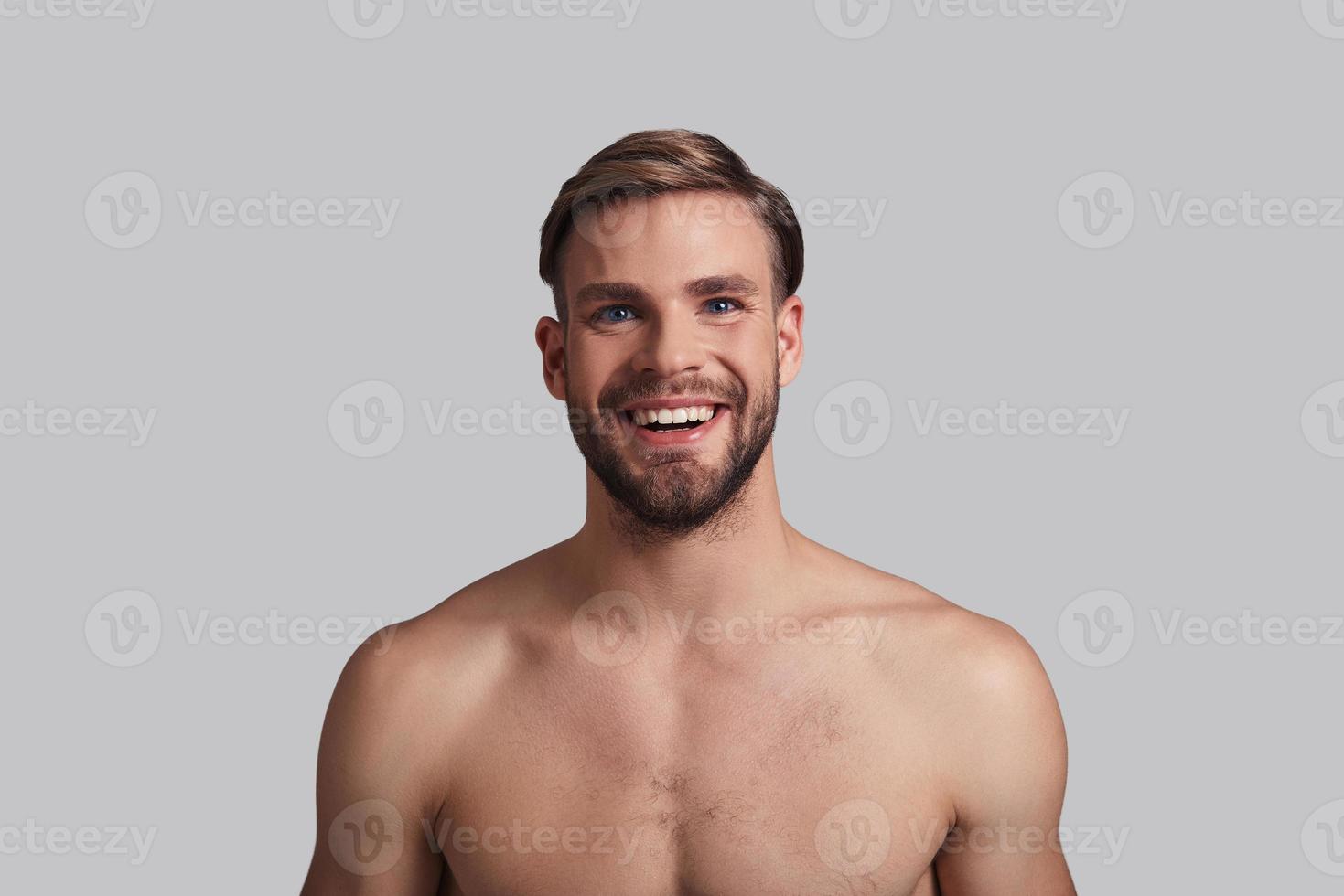 Perfect man. Handsome young man looking at camera and smiling while standing against grey background photo