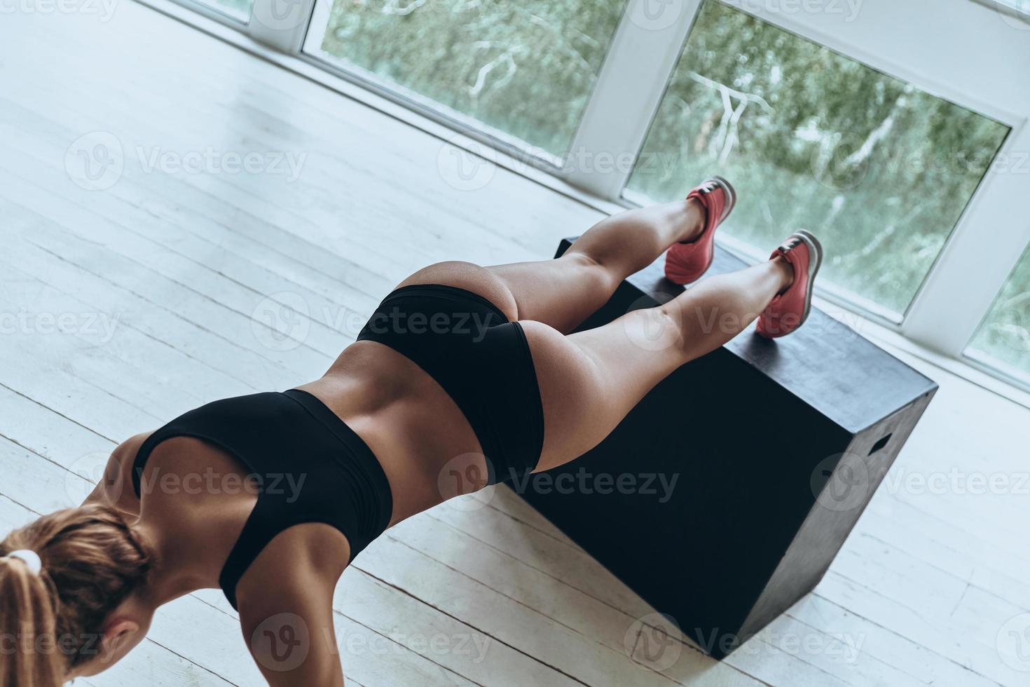 Working hard to be the best. Top view of young woman in sport clothing keeping plank position while exercising in the gym photo