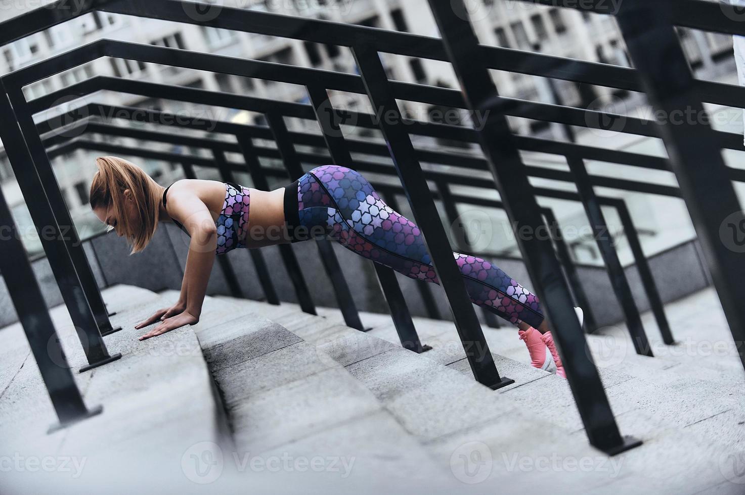 Sport is the way of her life. Modern young woman in sport clothing keeping plank position while exercising on the steps outdoors photo