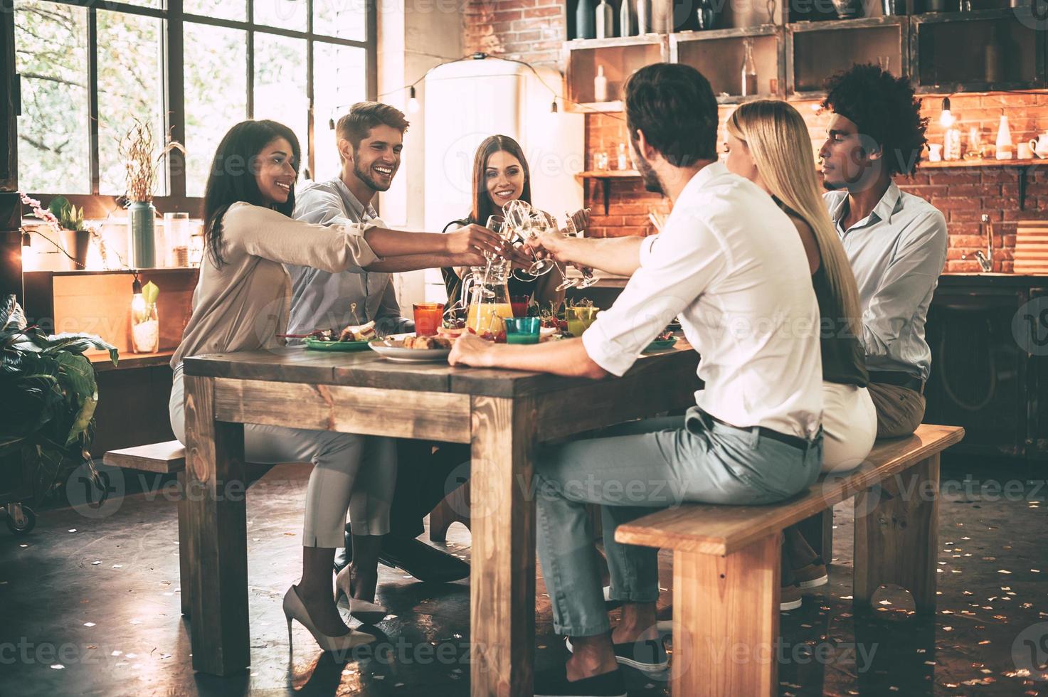 Cheers to us Group of cheerful young people cheering with champagne flutes and looking happy while while sitting at the dinning table together photo