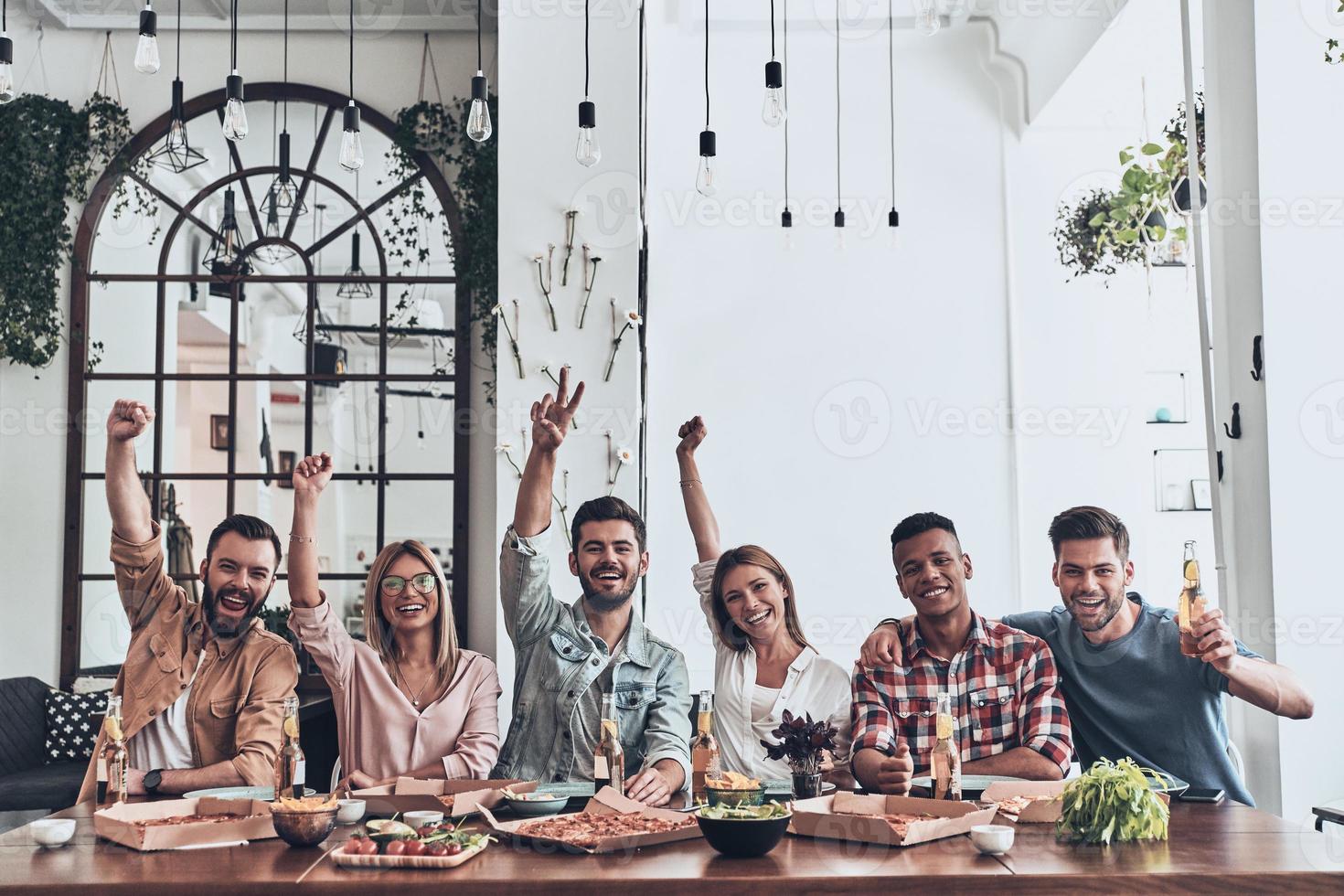Best friends ever. Beautiful young people in casual wear gesturing and smiling while having a dinner party indoors photo