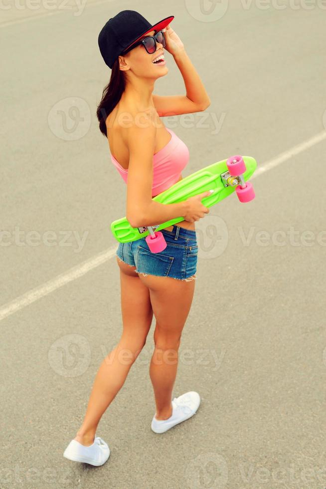 Time for skateboarding. Top view of beautiful young smiling woman holding her colorful skateboard and smiling while walking along the road photo