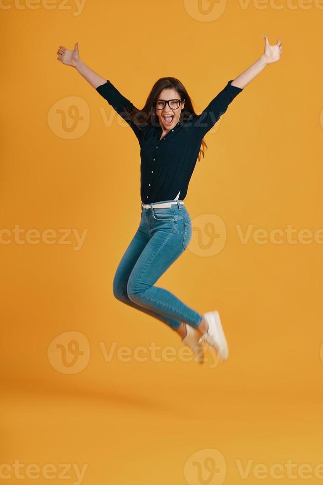 Full of length beautiful young women screaming and jumping against yellow background photo