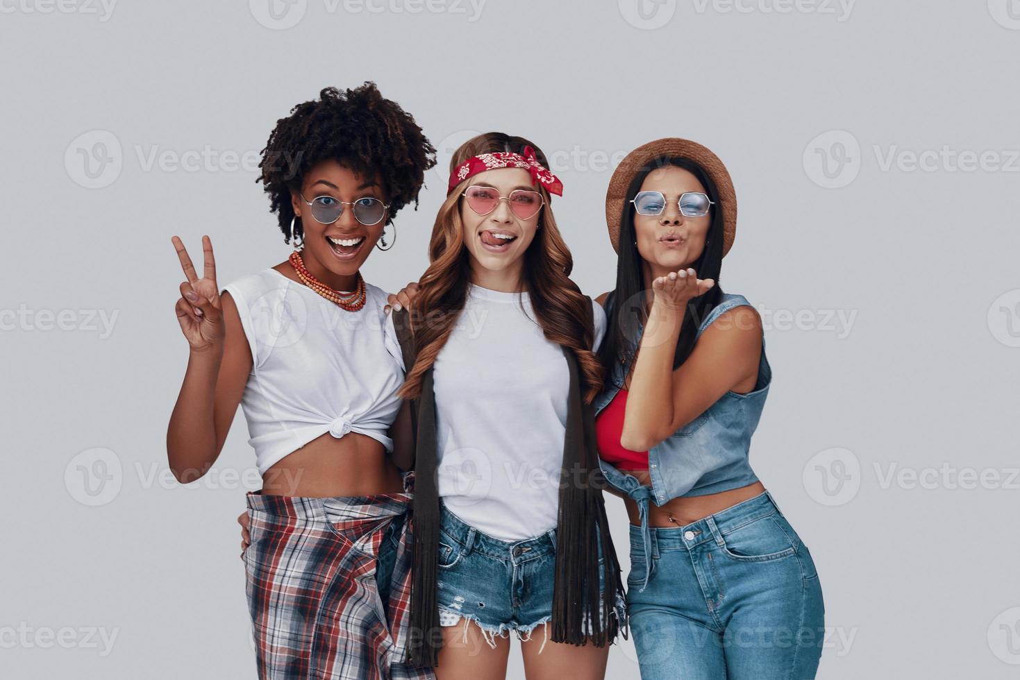 Three attractive young women smiling and looking at camera while standing against grey background photo