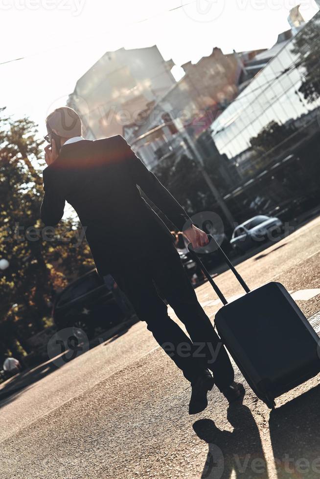 Business on the go. Full length rear view of young man in full suit talking on the phone while walking outdoors photo