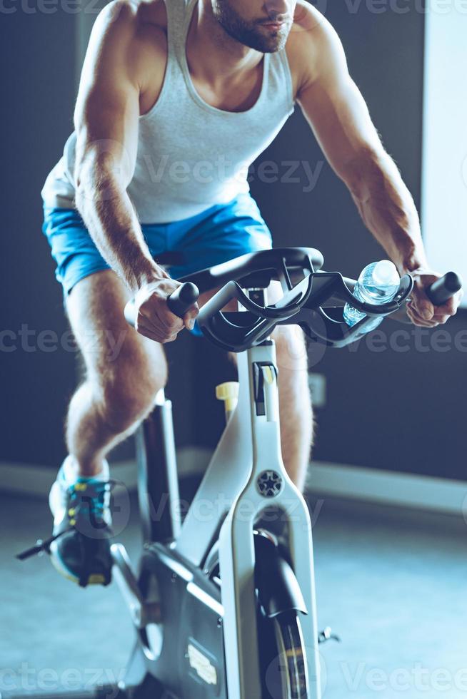 Best indoor machine for weight loss. Part of young man in sportswear cycling at gym photo