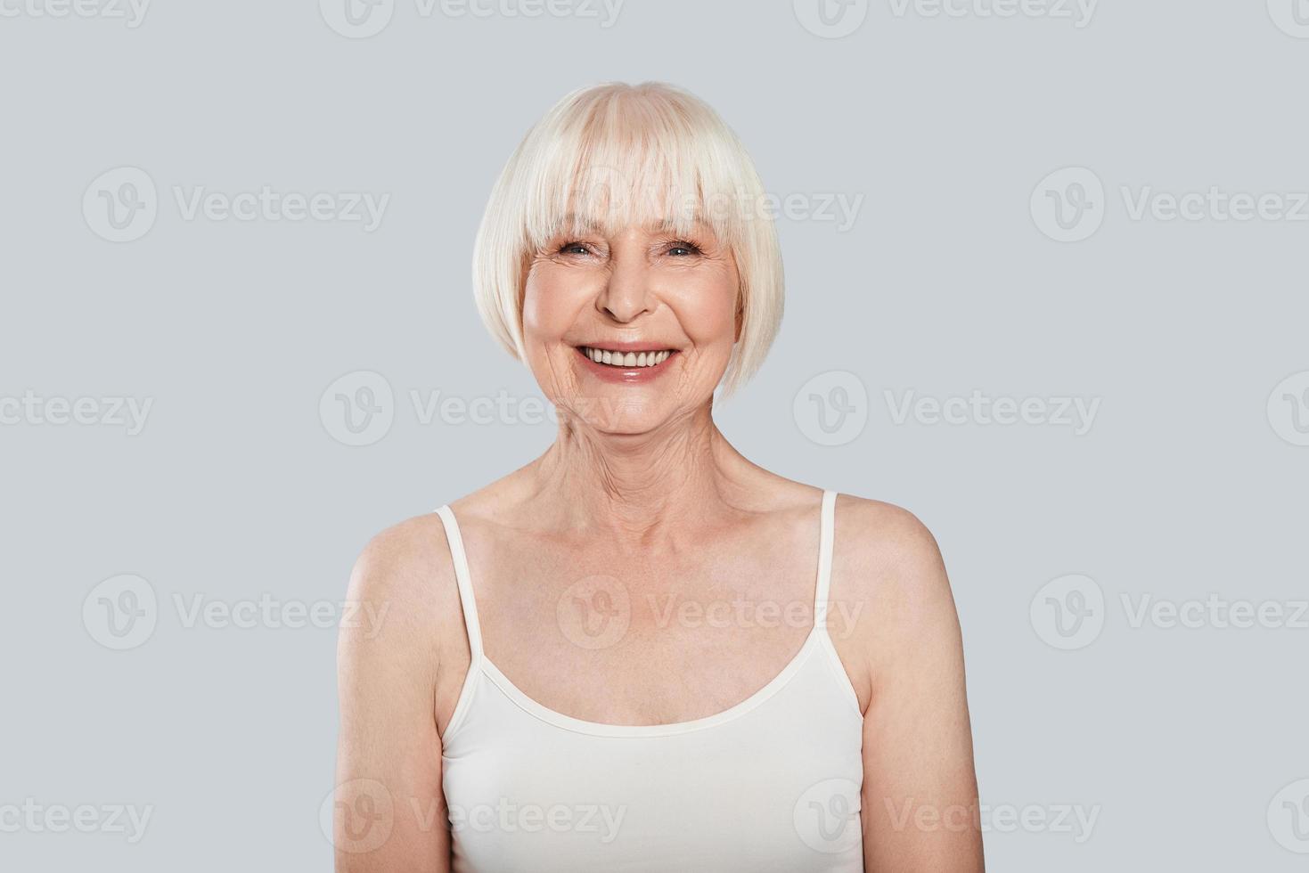 Natural beauty. Beautiful senior woman looking at camera and smiling while standing against grey background photo