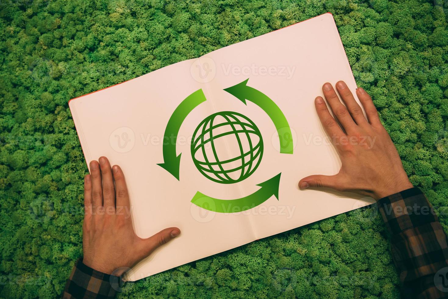 Protect the environment. Top view close-up image of man holding hands on his notebook with arrow and planet symbol at moss background photo