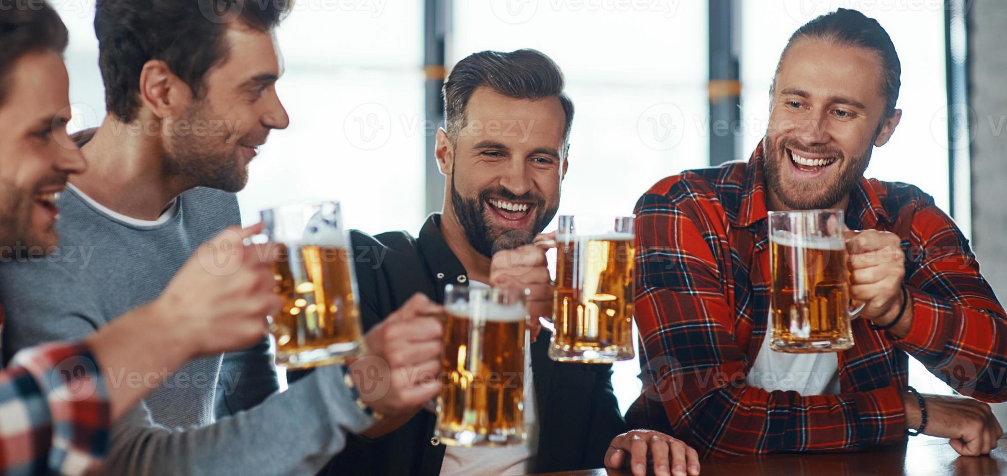 Happy young men in casual clothing toasting each other with beer and smiling photo