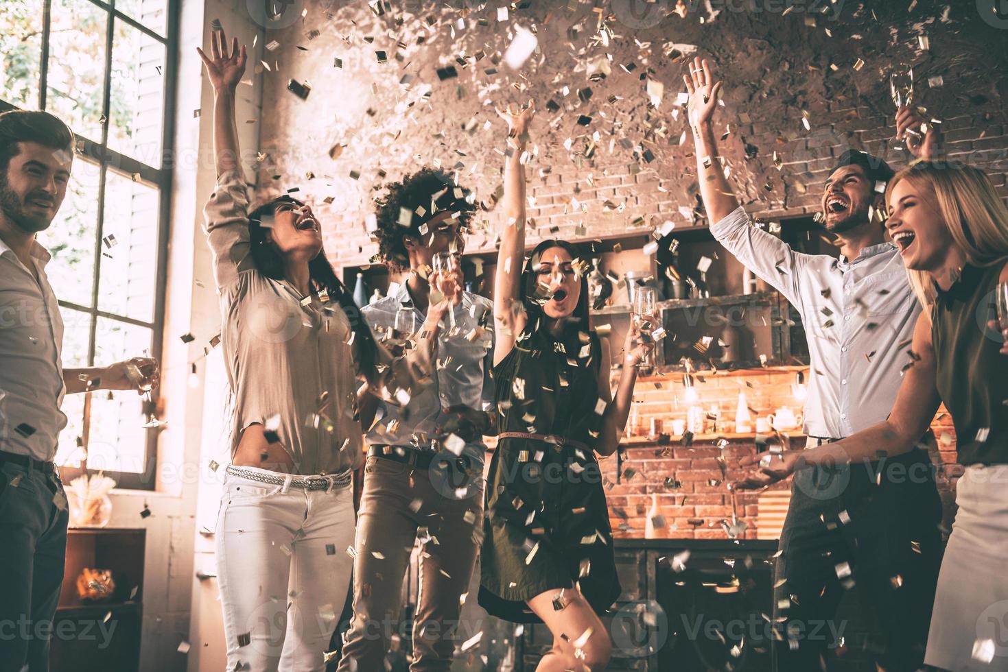 Confetti fun. Group of happy young people throwing confetti and jumping while enjoying home party on the kitchen photo