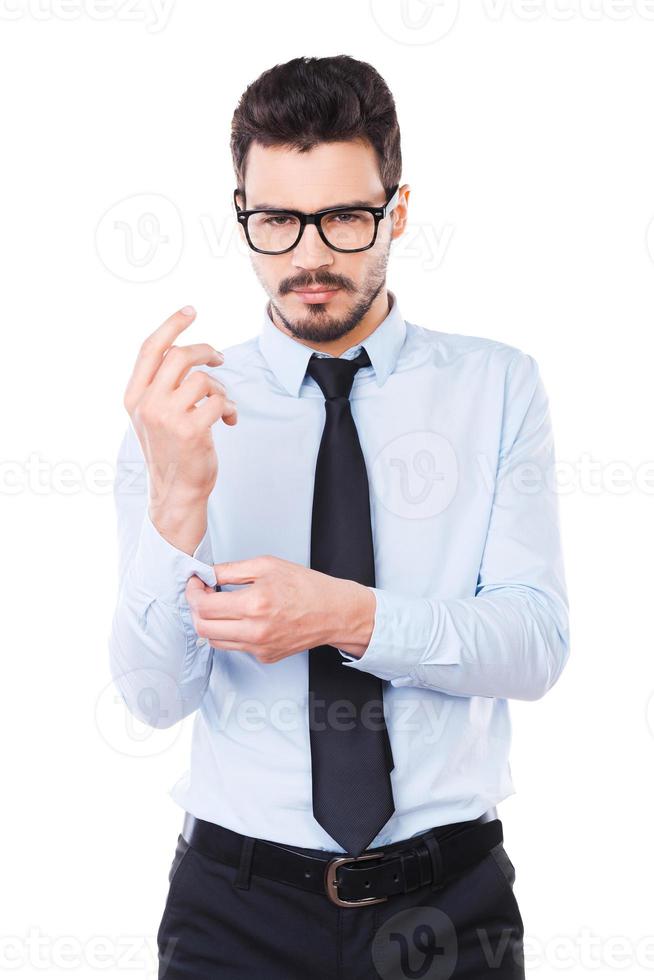 Used to success. Confident young man in shirt and tie looking at camera and adjusting his sleeve while standing against white background photo