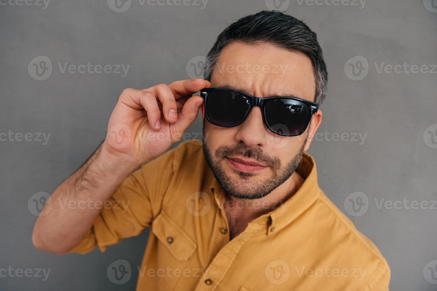 Well hello Top view of handsome young man adjusting his sunglasses and looking at camera while standing against grey background photo