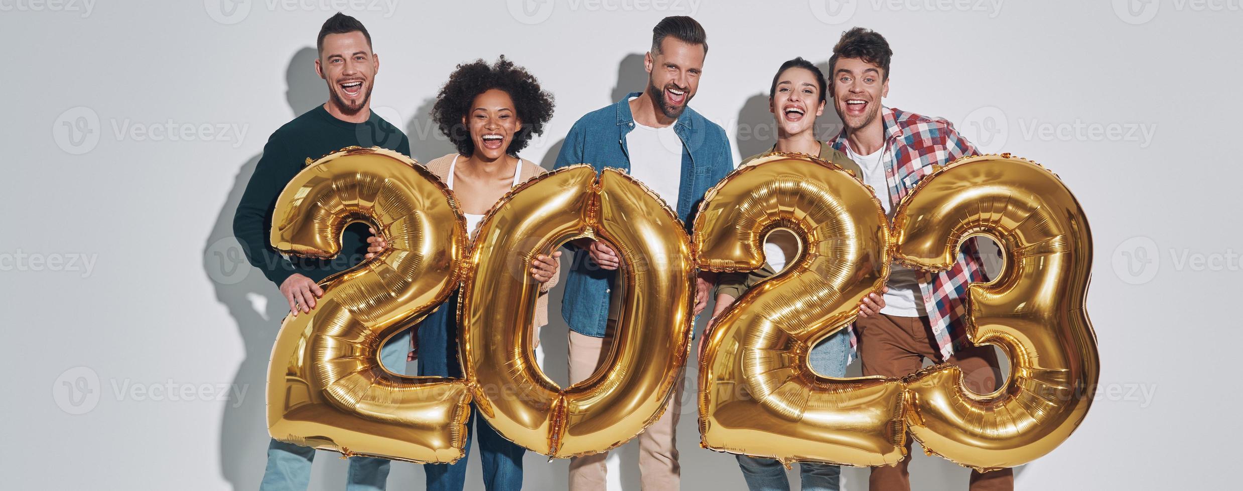 grupo de jóvenes hermosos con ropa informal que llevan números dorados y sonríen foto