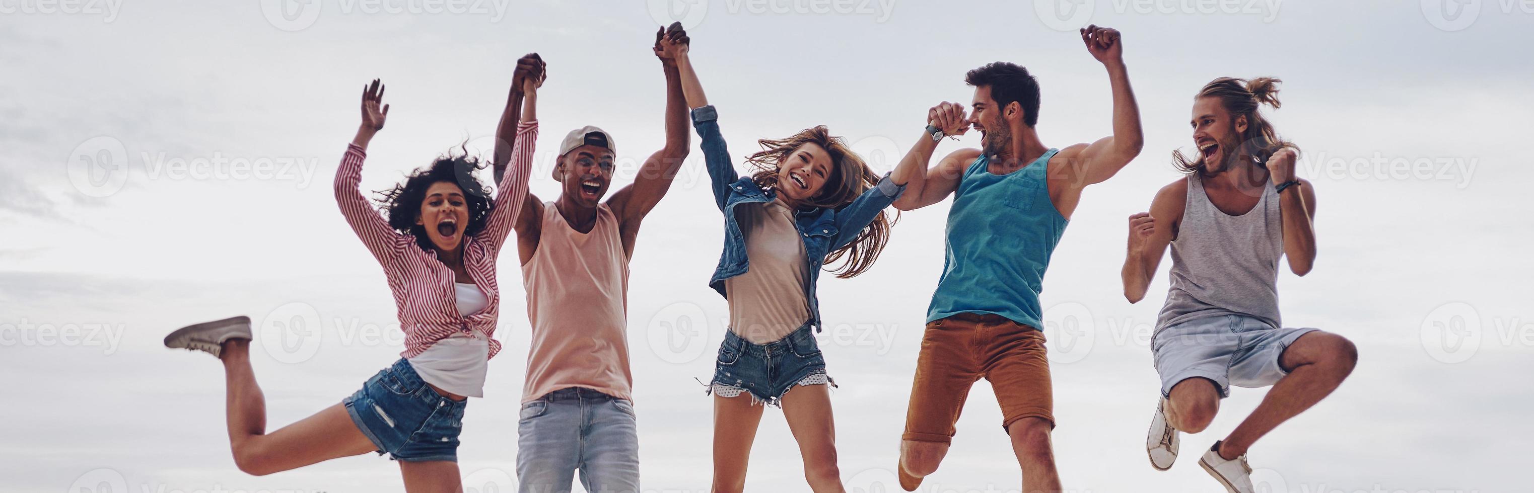 Life is better with friends. Full length of young people in casual wear smiling and gesturing while jumping on the pier photo