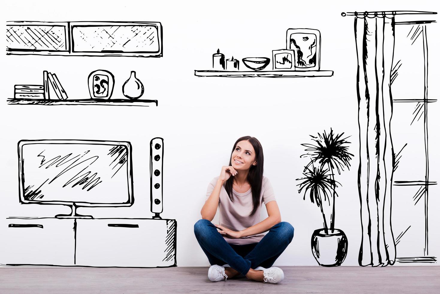 Dreaming about new apartment. Cheerful young woman smiling while sitting on the floor against white background with drawn home interior photo