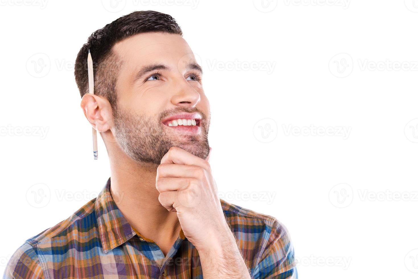 Generating new ideas. Thoughtful young male carpenter holding hand on chin and looking away with smile while standing against white background photo