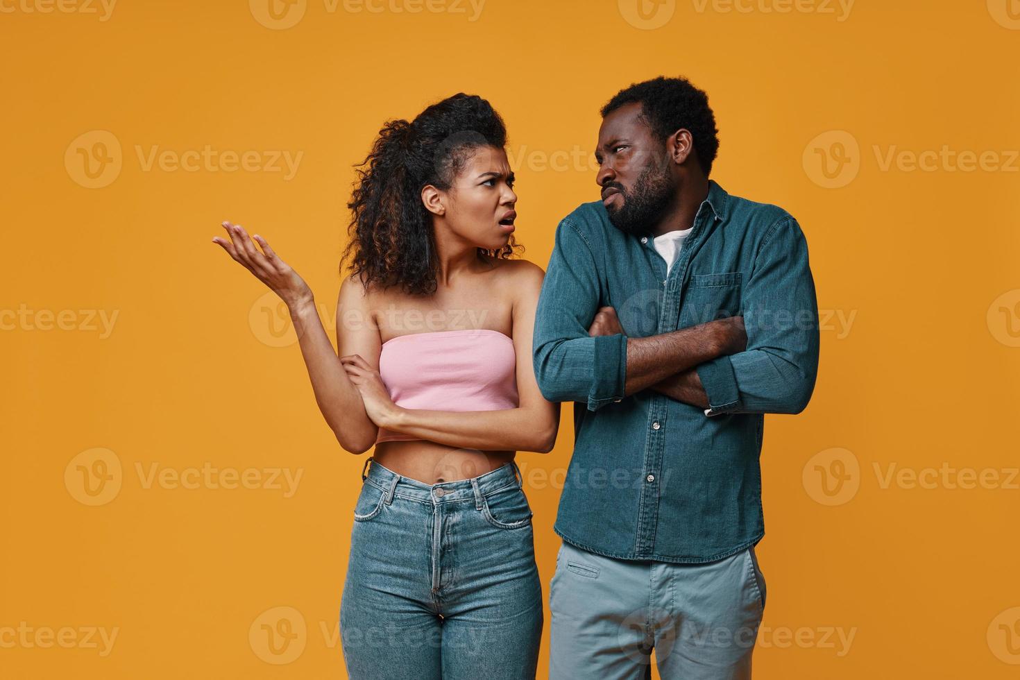 Young African couple gesturing and having conflict while standing against yellow background photo