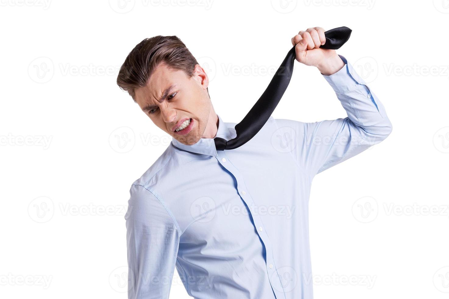 Tired of office life. Portrait of frustrated young man in formalwear stretching out his necktie and grimacing while standing isolated on white photo