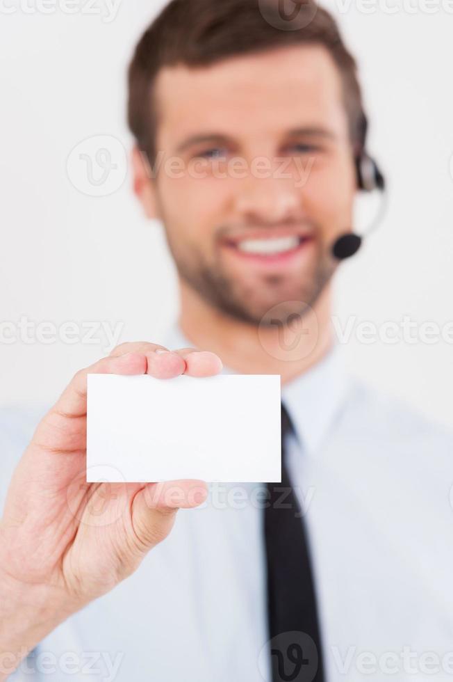 Call this number Handsome young man in formalwear and headset stretching out a business card and smiling while standing isolated on white background photo