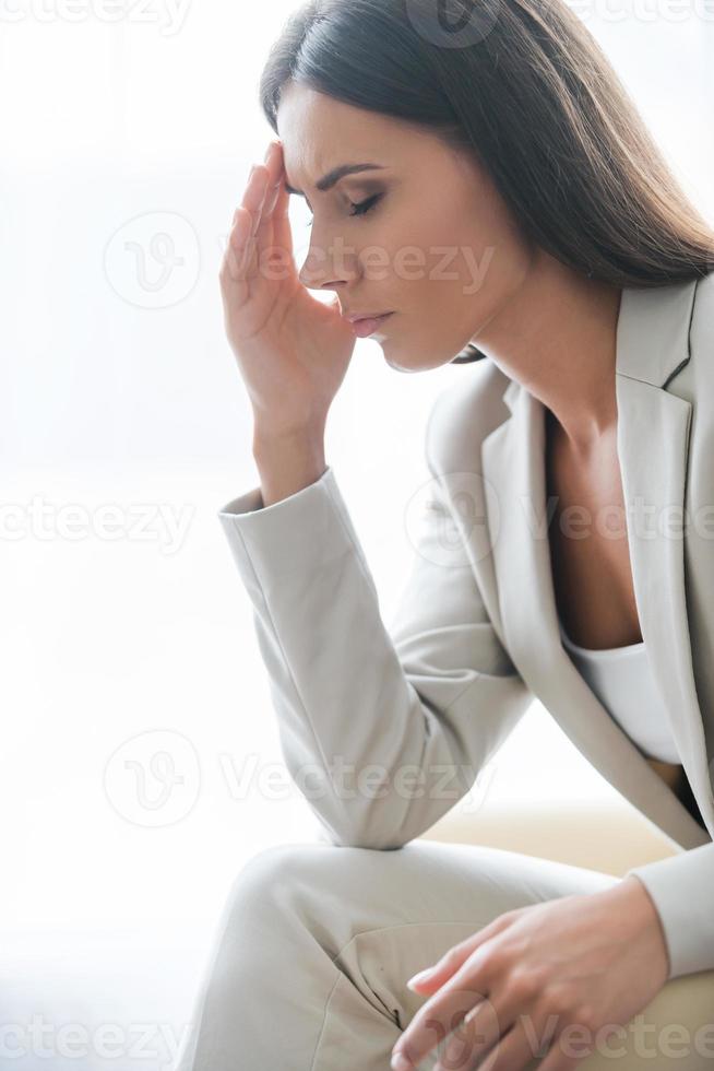 Depressed businesswoman. Side view of depressed young businesswoman in suit touching head with hand and keeping eyes closed while sitting at the chair photo