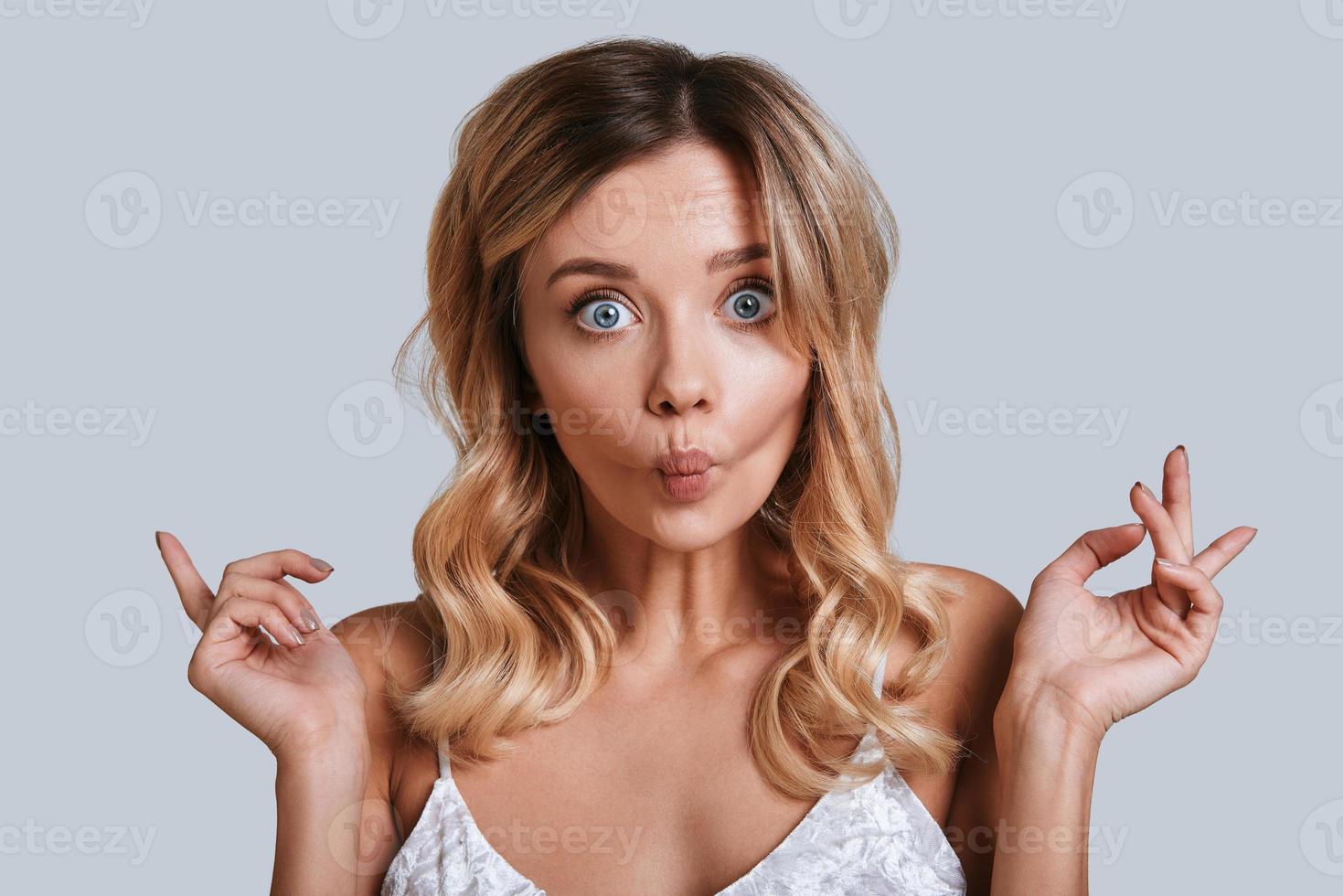 Incredible girl. Playful young woman looking at camera and making a face while standing against grey background photo