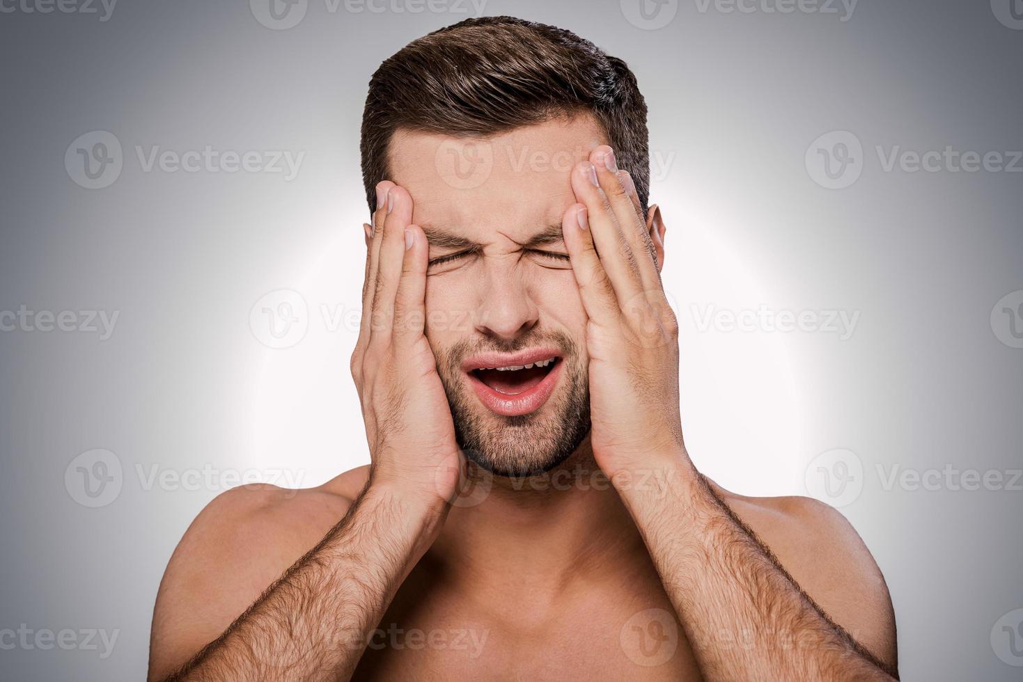 This awful headache Portrait of frustrated young shirtless man touching head with hands and keeping eyes closed while standing against grey background photo