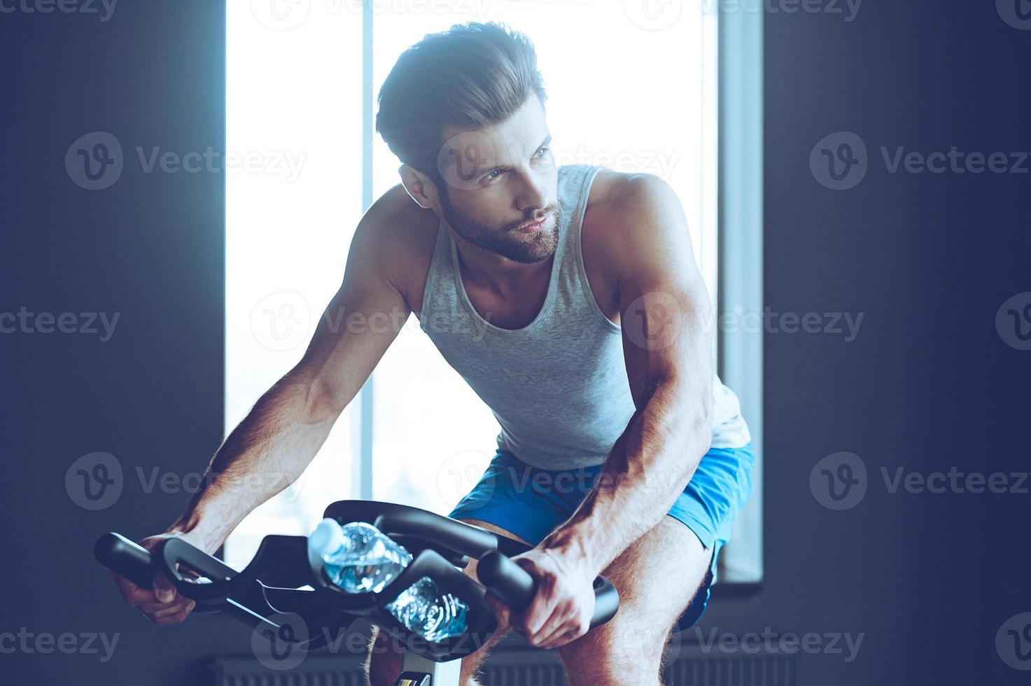 ciclismo duro. joven apuesto en ropa deportiva mirando hacia otro lado mientras anda en bicicleta en el gimnasio foto