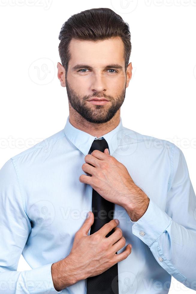 Used to look perfect. Confident young handsome man adjusting his necktie and looking at camera while standing against white background photo