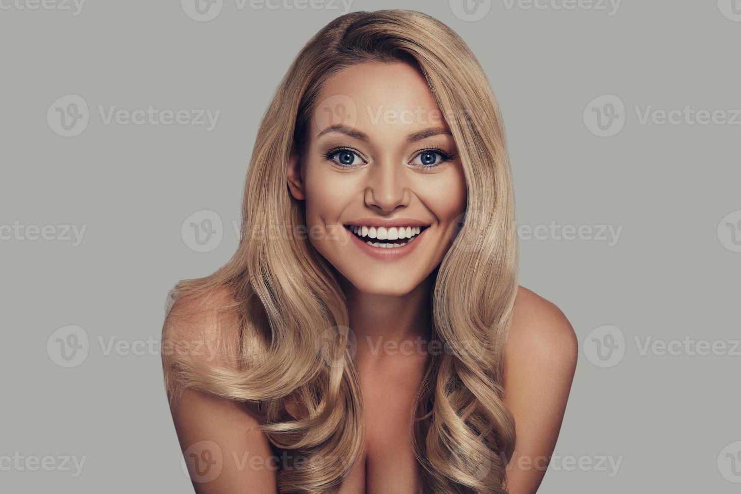 Incredible Beautiful young woman smiling and looking at camera while standing against grey background photo