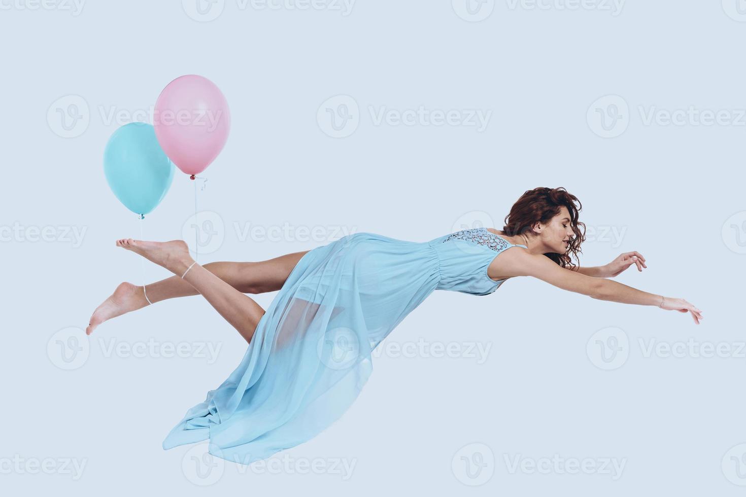 mosca de ensueño. foto de estudio de una joven atractiva con un vestido elegante que mantiene los brazos extendidos mientras se cierne sobre un fondo gris
