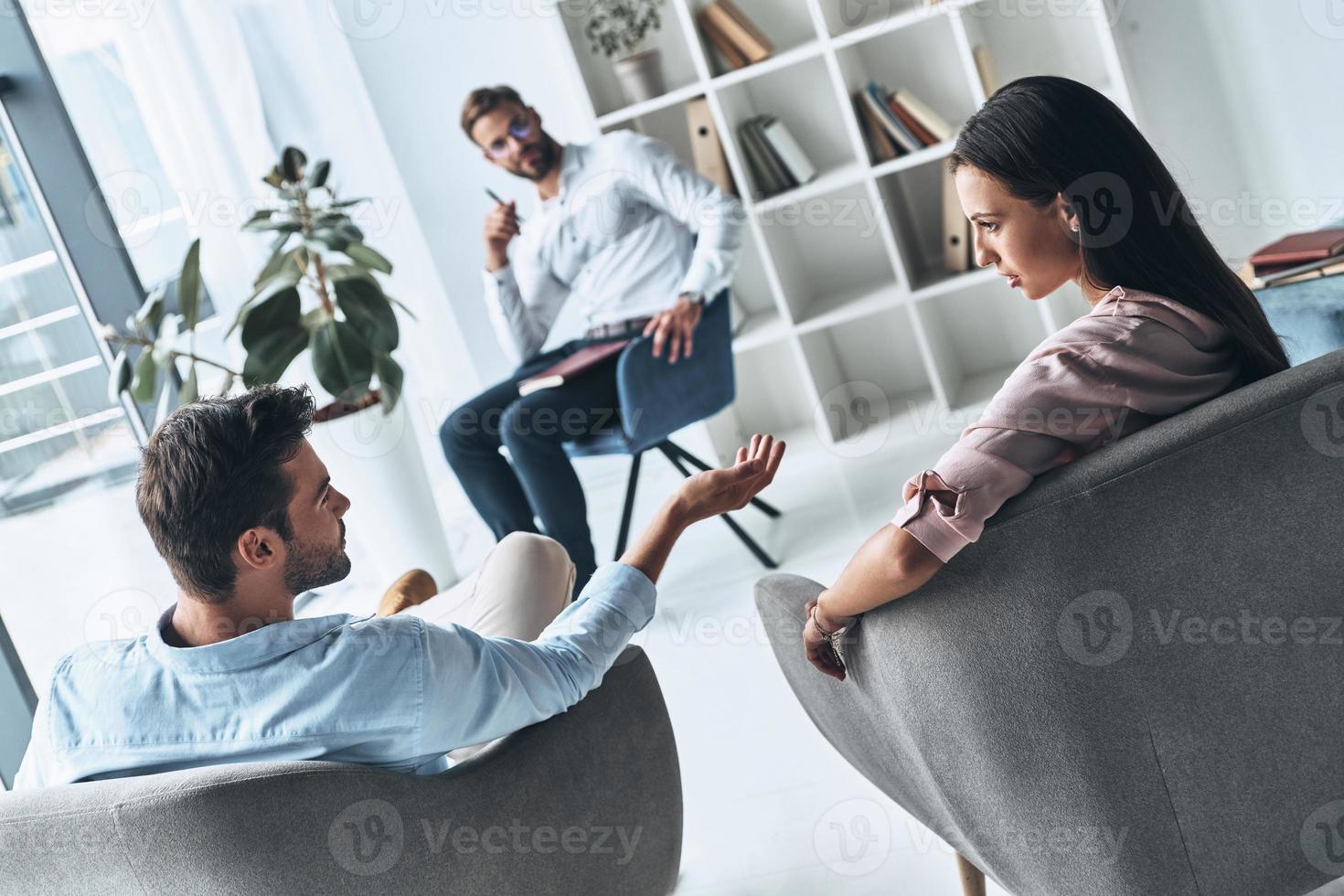 Trying to understand both sides. Young married couple talking while sitting on the therapy session with psychologist photo