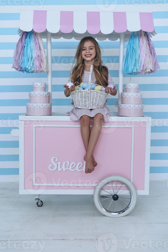 Happy about Easter.  Cute little girl holding Easter eggs and smiling while sitting on the candy cart decoration photo