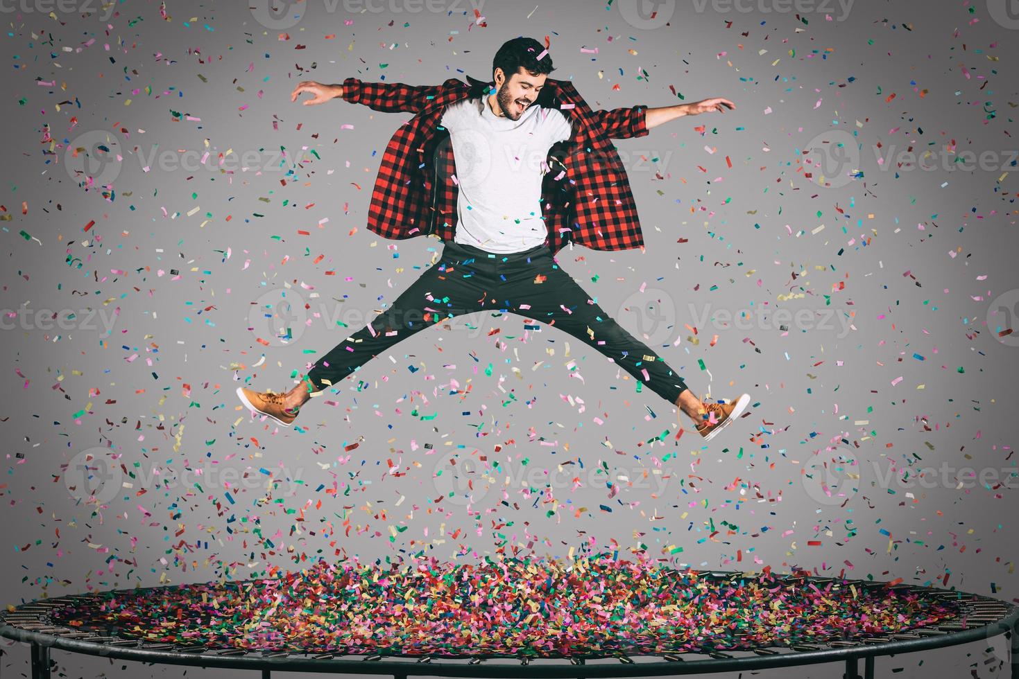 Carefree fun. Mid-air shot of handsome young man jumping on trampoline with confetti all around him photo