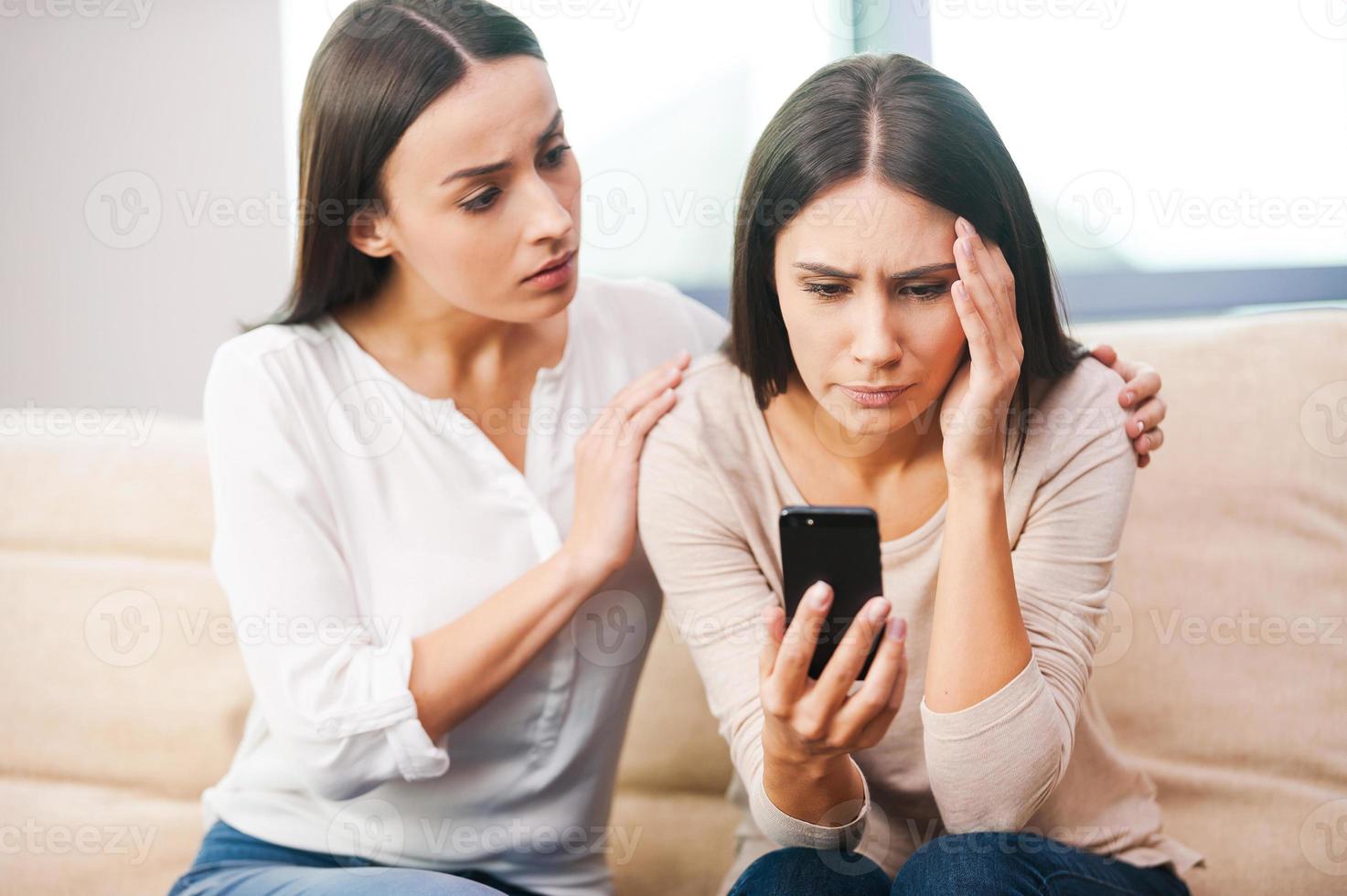 Real friends are always near. Depressed young woman holding mobile phone while being consoled by her friend photo