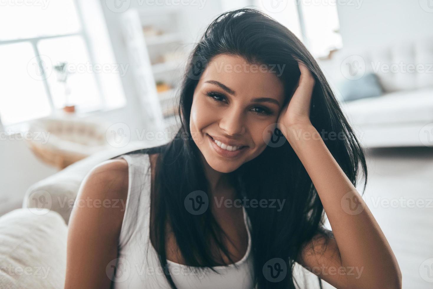 Beautiful and charming. Portrait of attractive young woman looking at camera and smiling while sitting on the couch at home photo