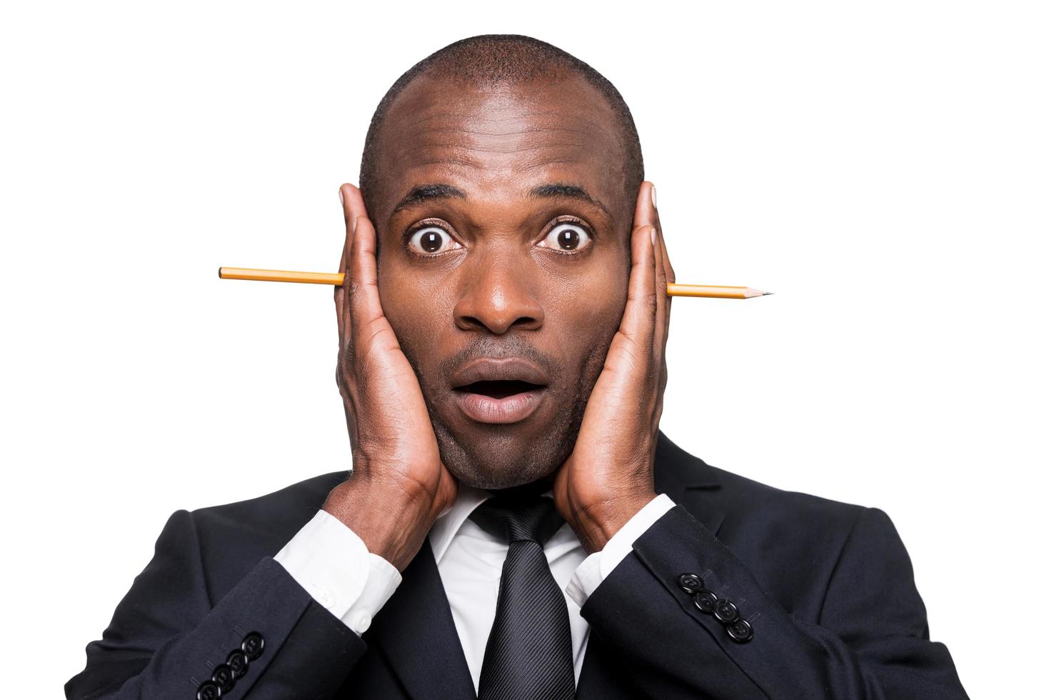 Something wrong... Surprised young African man in formalwear holding head in hands with pencil sticking out of it while standing isolated on white background photo