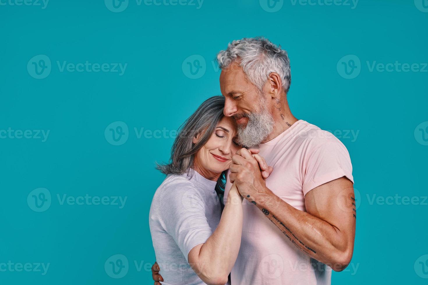 una pareja romántica de ancianos bailando y sonriendo mientras están juntos contra el fondo azul foto