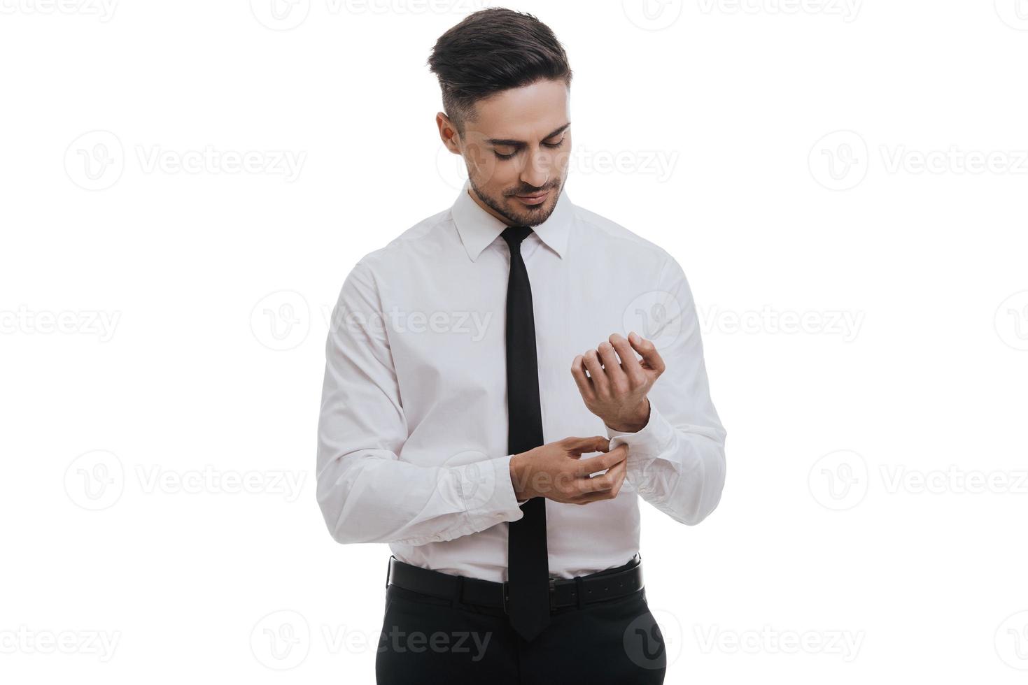 Preparing to new achievements. Good looking young man in white shirt and tie adjusting his sleeve while standing against grey background photo