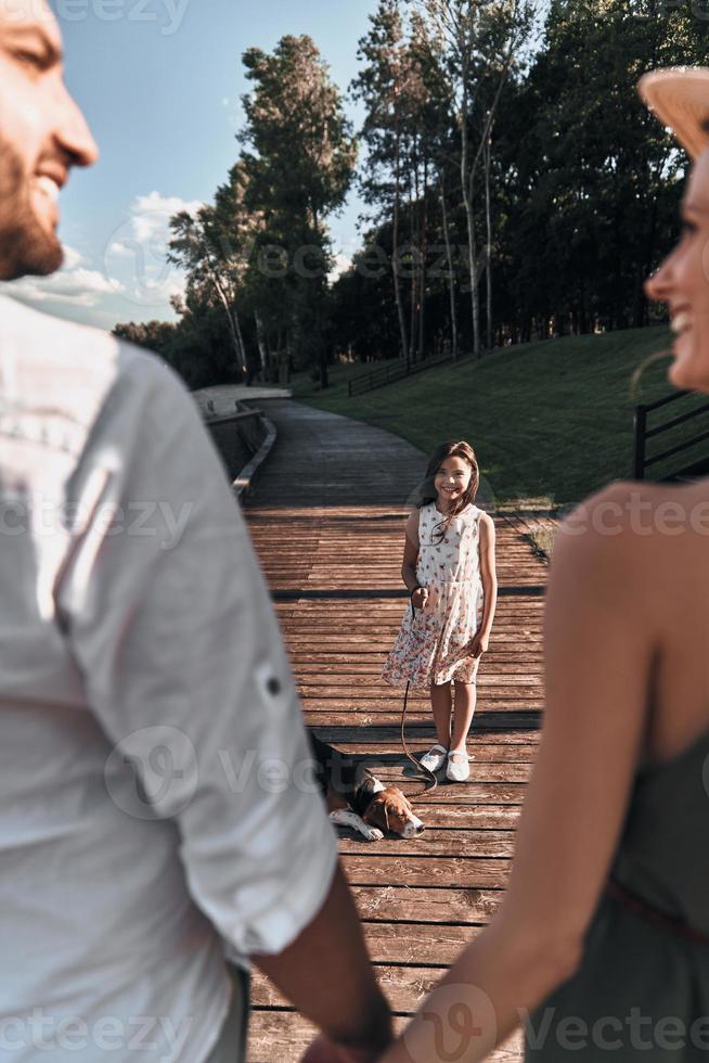 Young parents looking at each other and holding hands while their daughter standing in front of them with dog photo