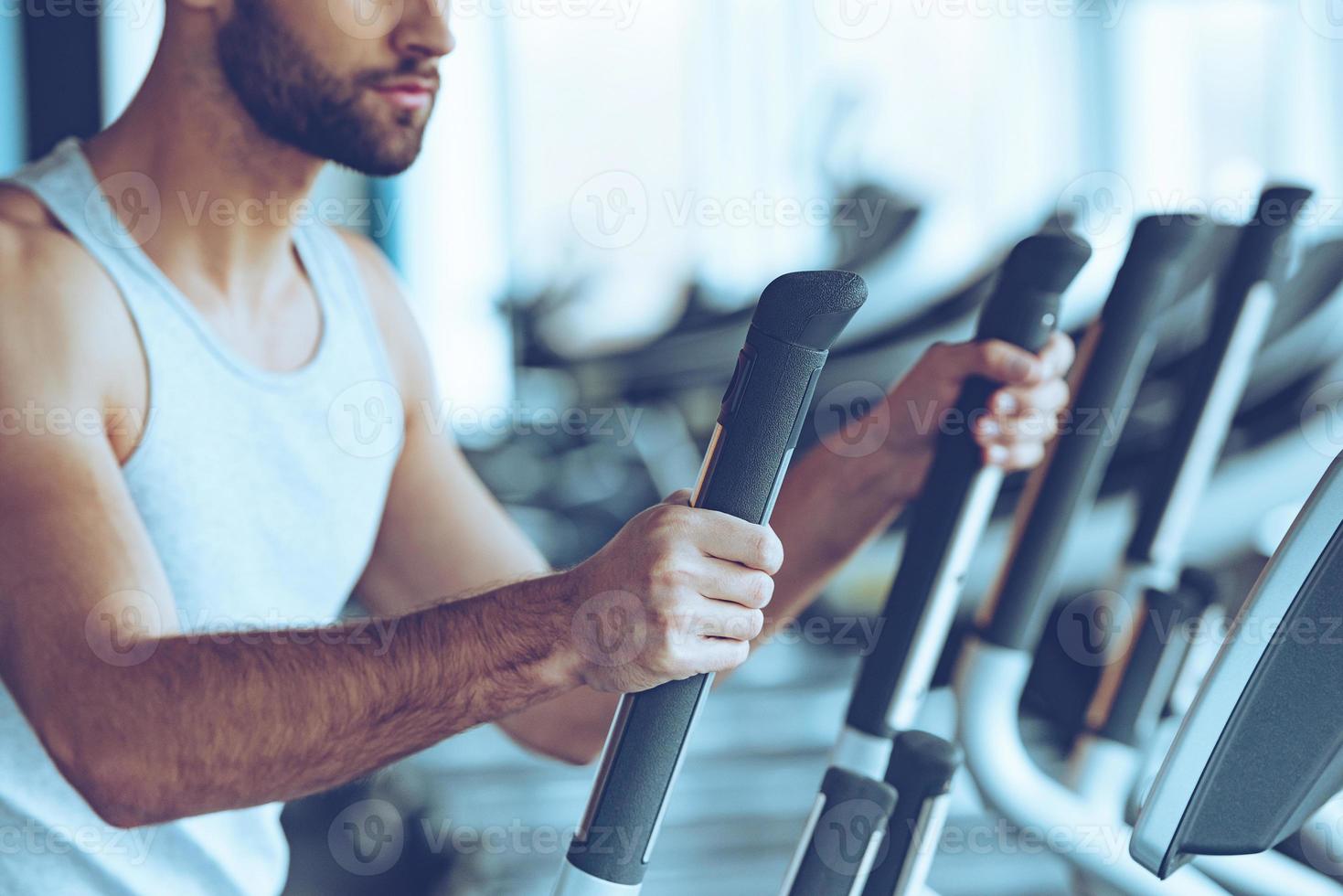 Working out. Side view close-up part of young man in sportswear working out on stepper at gym photo
