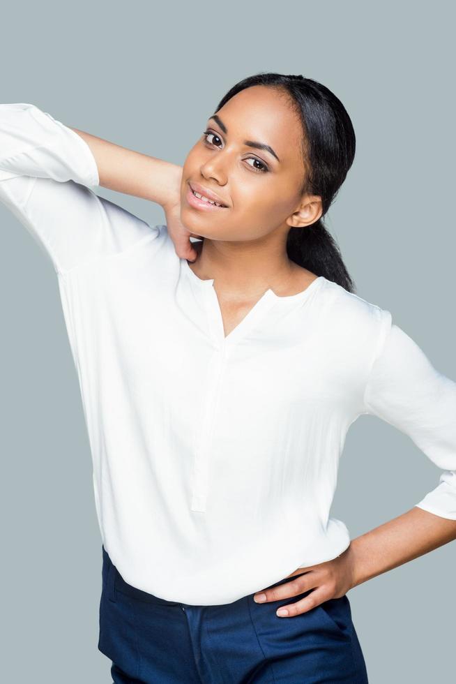 Confident beauty. Attractive young African woman holding hands on hip and looking at camera while standing against grey background photo