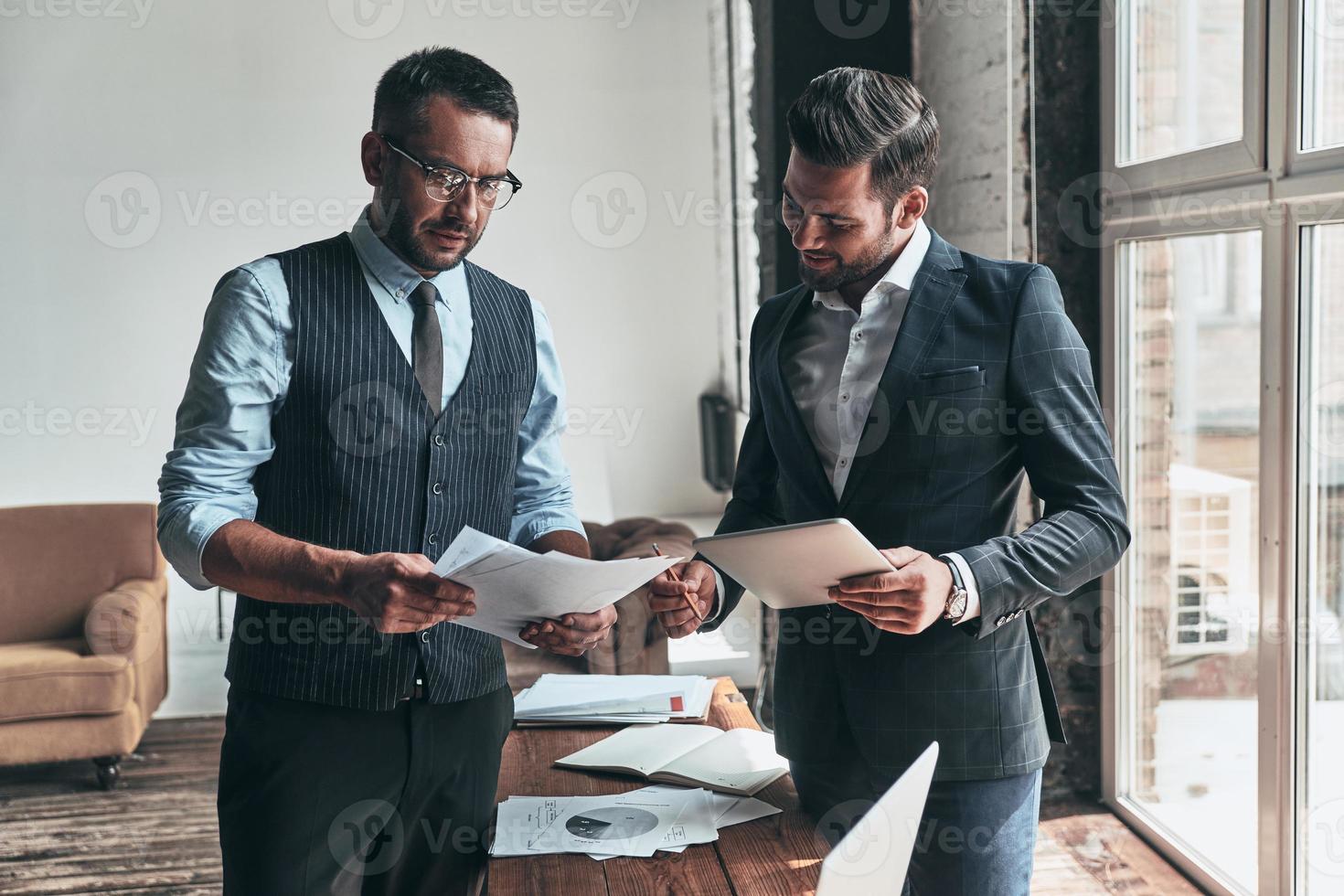 Sharing new ideas. Two young modern men in formalwear working together while standing indoors photo