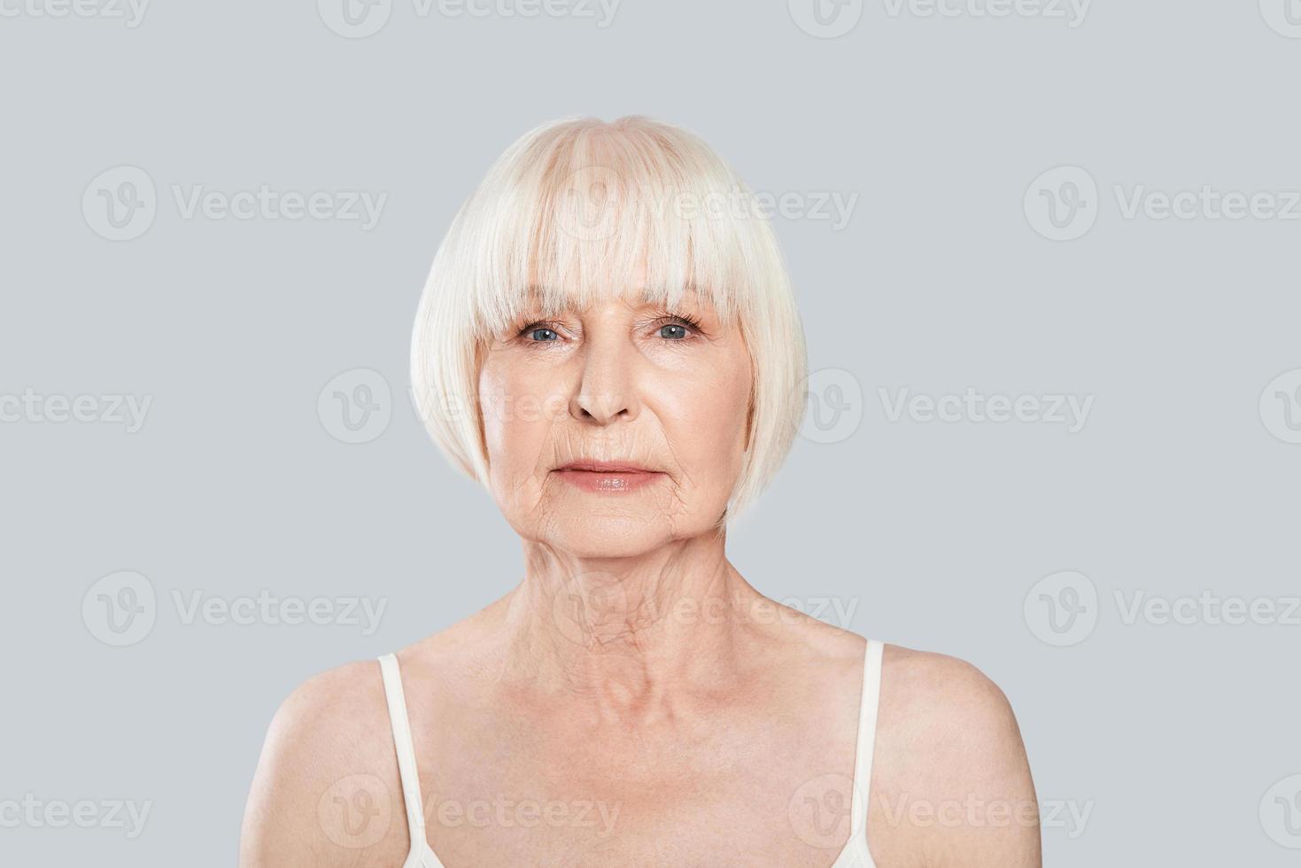 Human age. Beautiful senior woman looking at camera while standing against grey background photo