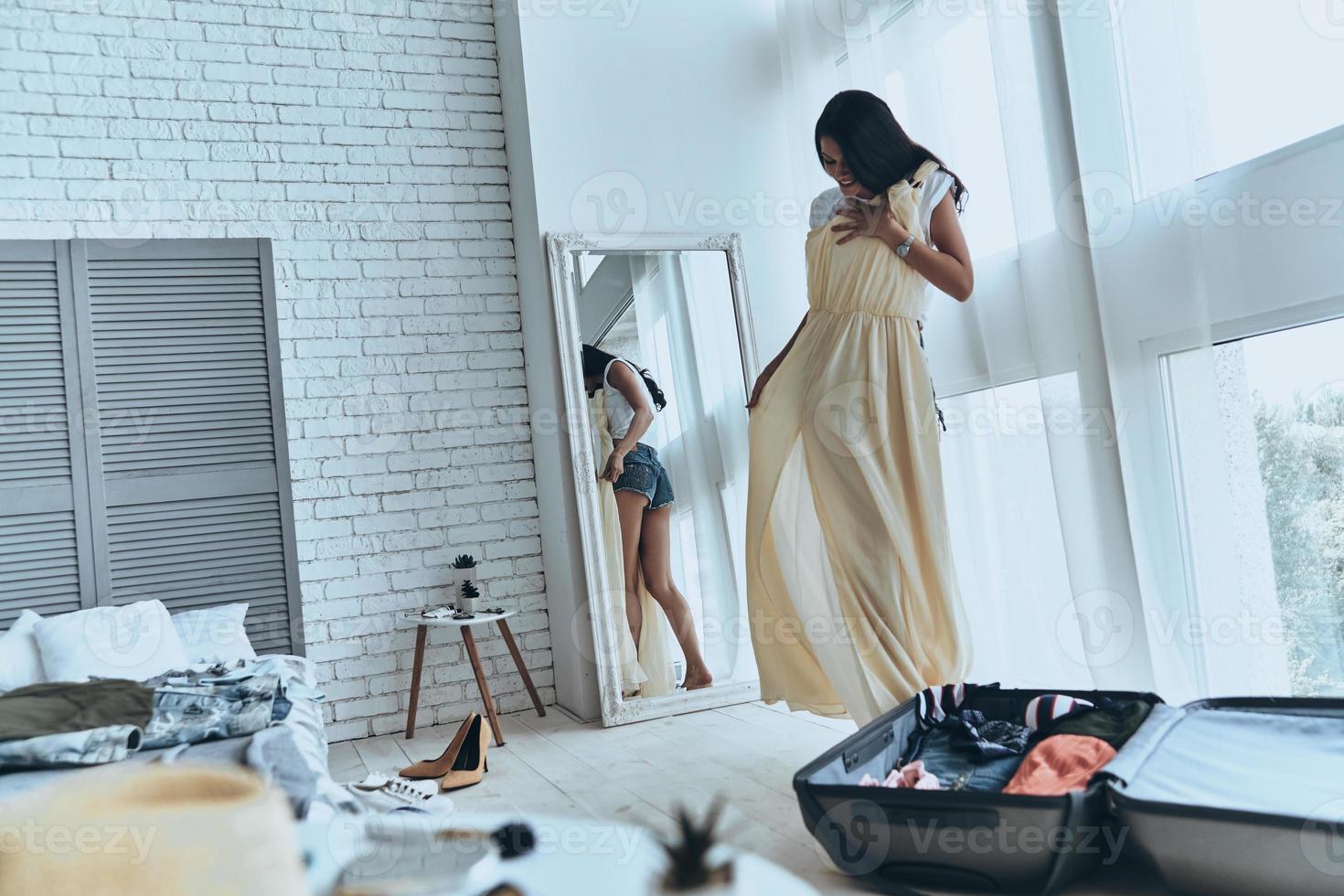 Full length of attractive young woman trying on her dress and smiling while standing near the mirror at home photo