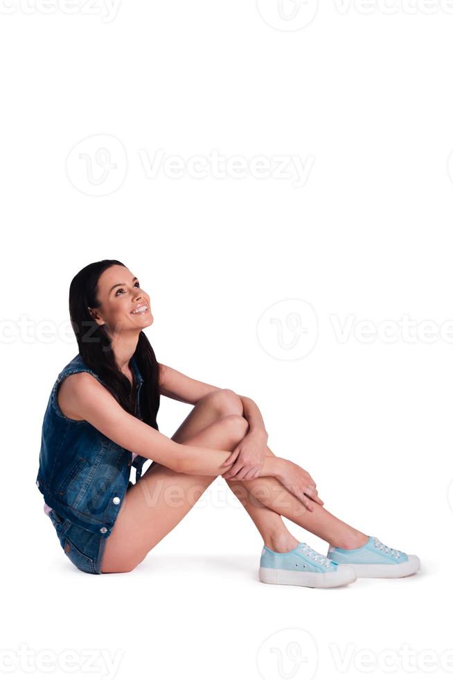 In great mood. Beautiful young cheerful woman looking up with smile while sitting against white background photo